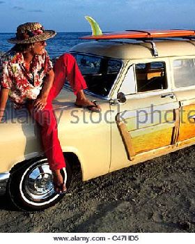 a-california-surfer-relaxes-on-his-woodie-station-wagon-as-the-sun-c47hd5