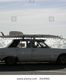 old-convertible-car-with-surfboard-on-roof-driving-on-esplanade-A5HM6E
