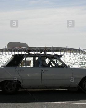 old-convertible-car-with-surfboard-on-roof-driving-on-esplanade-A5HM6E